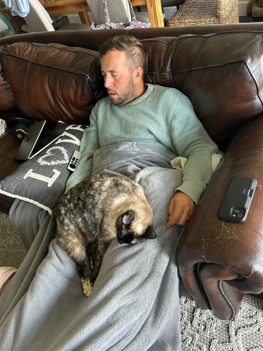 Carl asleep on the couch under a blanket, the family cat asleep on top