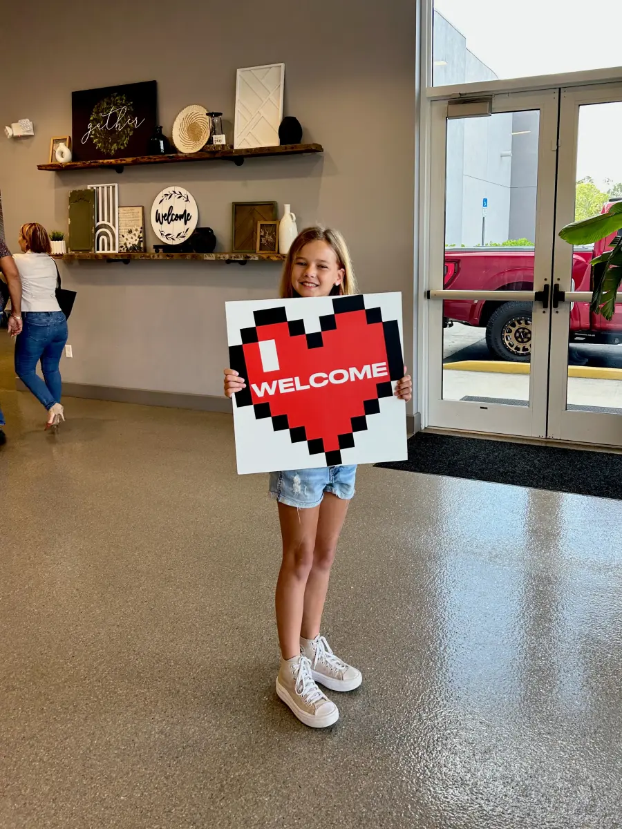 Amelia holding a pixel-heart Welcome sign at the church door