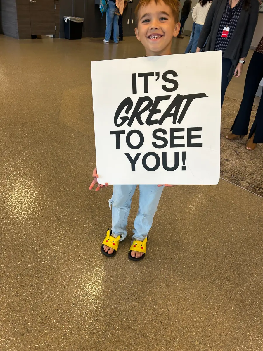 Duke grinning behind a sign that says It's great to see you