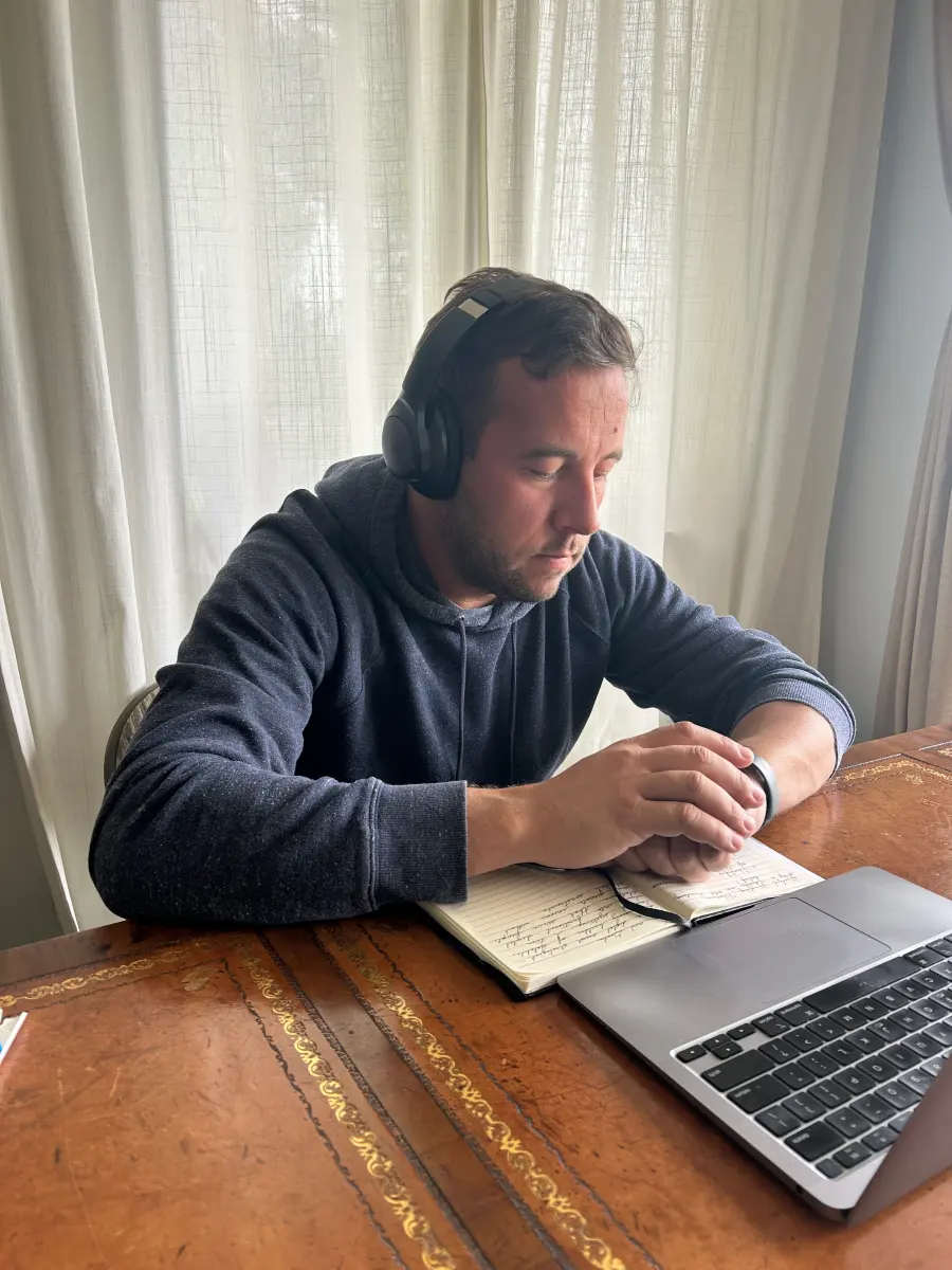 Carl at his desk with headphones on, a notebook open beside the laptop