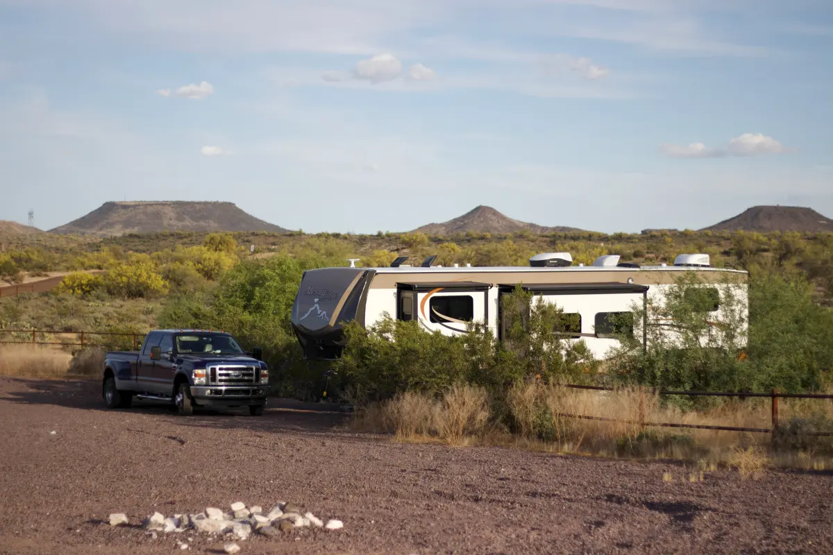 A fifth-wheel trailer and a pickup truck parked in the desert