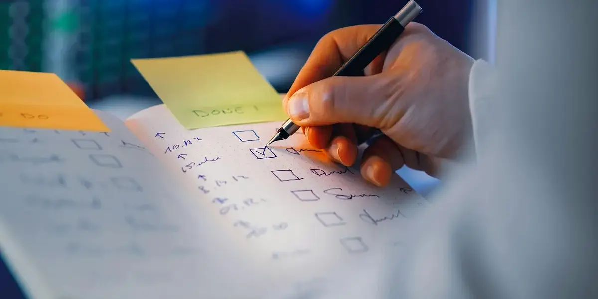 Close-up of a hand writing in a notebook with checkboxes, highlighting productivity and organization.