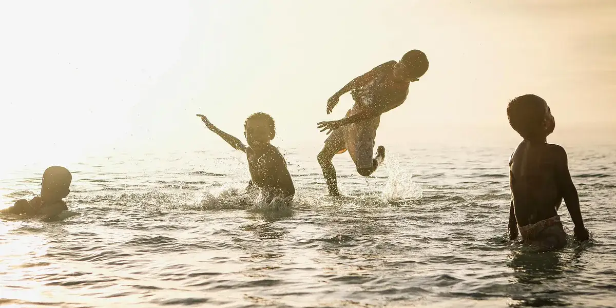 Young kids having fun splashing in the sea with sunlit background.