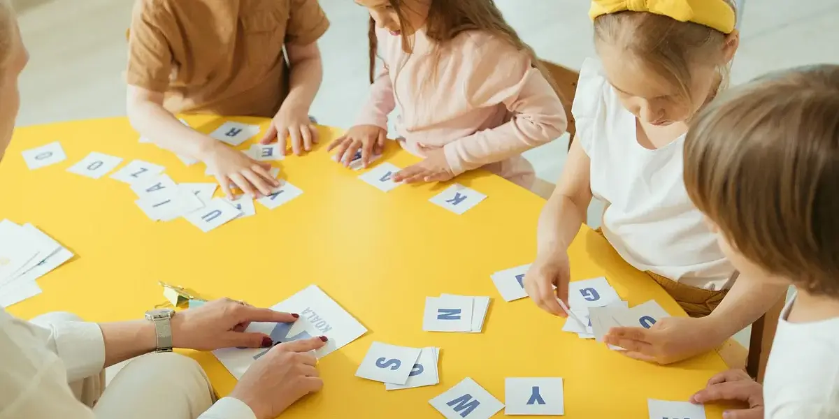 Group of children engaging with alphabet cards on a bright yellow table for learning.