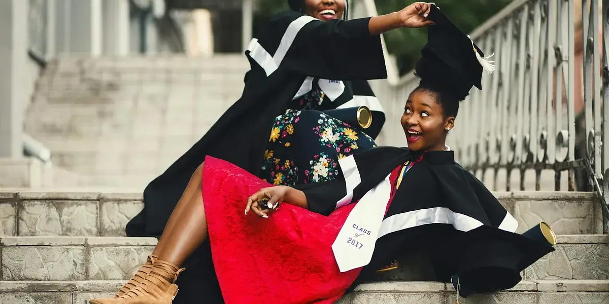 Two women in graduation gowns celebrating on stairs, embodying happiness and achievement.