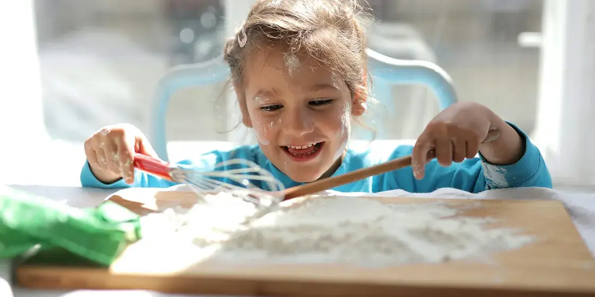 Smiling girl playing with flour and kitchen tools indoors. Captures innocence and fun.