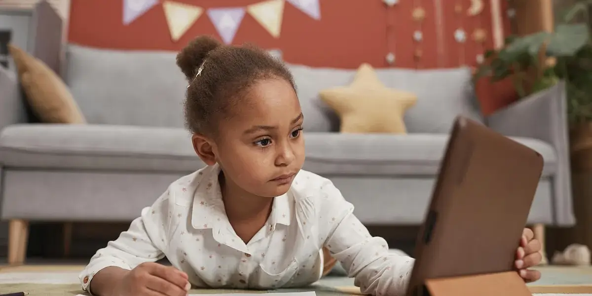 A young girl focused on learning online with a tablet in a cozy home setting.